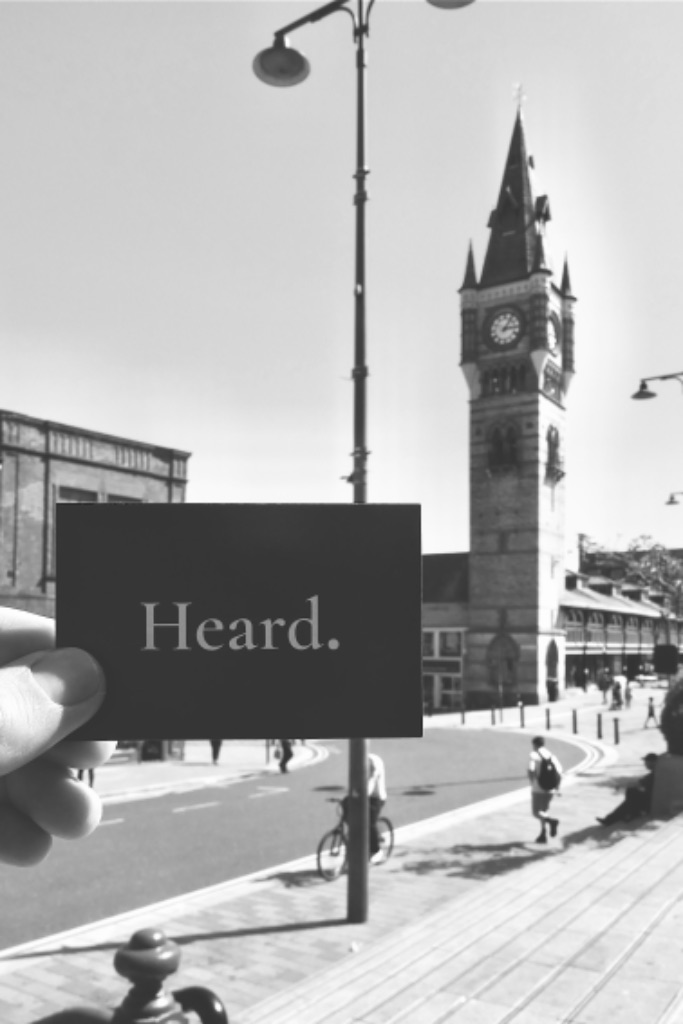 A Heard. business card held up in Darlington town centre, clock tower behind